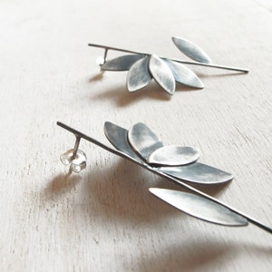 May include: A pair of silver earrings with a leaf design. The earrings are made of metal and have a long, thin stem with multiple leaves attached to it.
