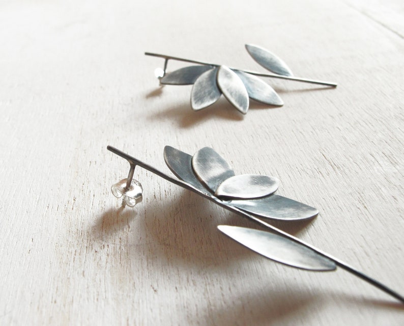 May include: A pair of silver earrings with a leaf design. The earrings are made of metal and have a long, thin stem with multiple leaves attached to it.