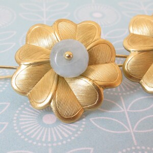 May include: A pair of gold flower-shaped earrings with a light blue stone in the center of each flower.