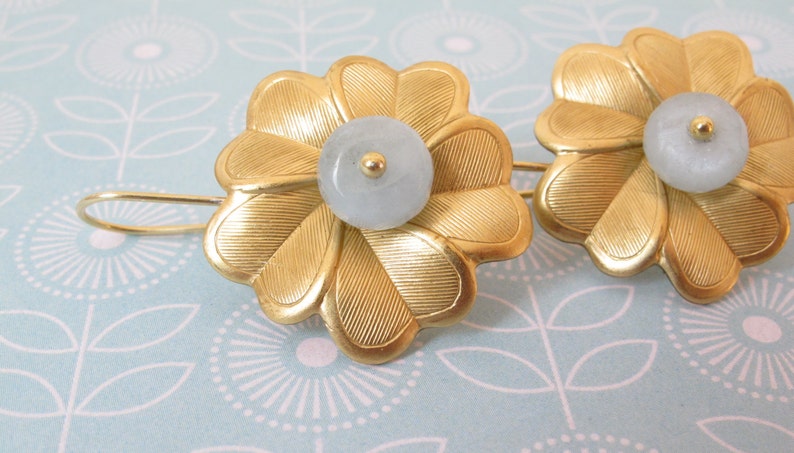 May include: A pair of gold flower-shaped earrings with a light blue stone in the center of each flower.