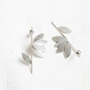 May include: A pair of silver earrings with a leaf design. One earring has a single leaf, while the other has multiple leaves.