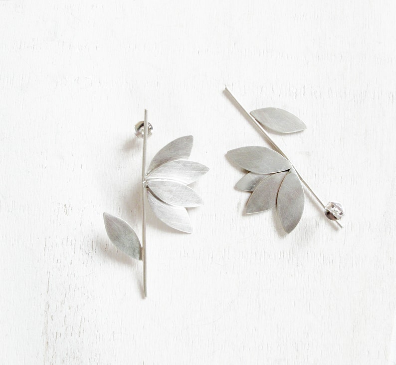 May include: A pair of silver earrings with a leaf design. One earring has a single leaf, while the other has multiple leaves.