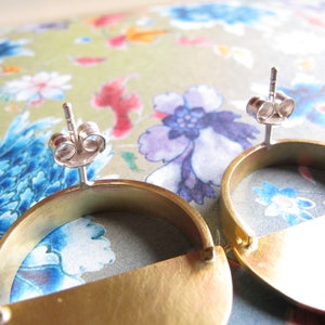 May include: A pair of gold-toned earrings with a half-circle design. The earrings have a silver post and butterfly back.