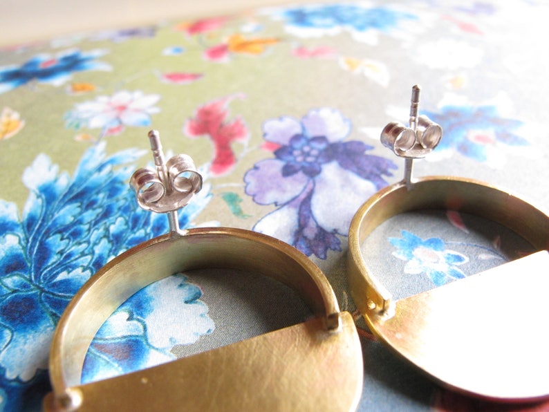 May include: A pair of gold-toned earrings with a half-circle design. The earrings have a silver post and butterfly back.