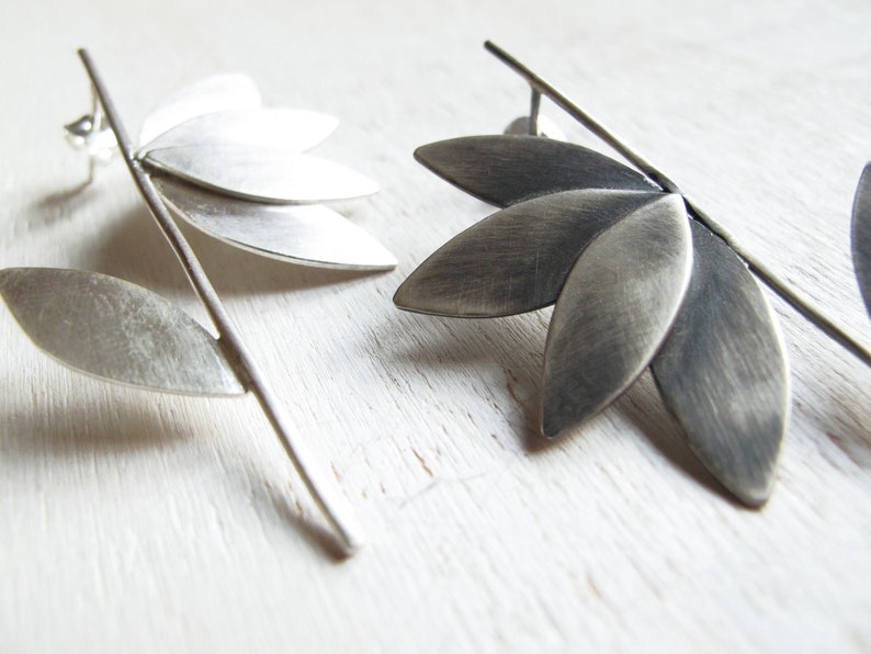 May include: A pair of silver earrings with a leaf design. The earrings are made of metal and have a brushed finish.