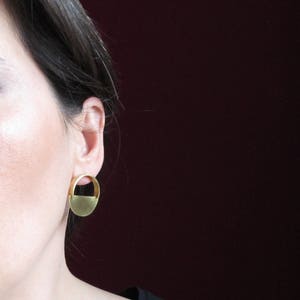 May include: A pair of gold-toned earrings with a half-circle design. The earrings are simple and modern.