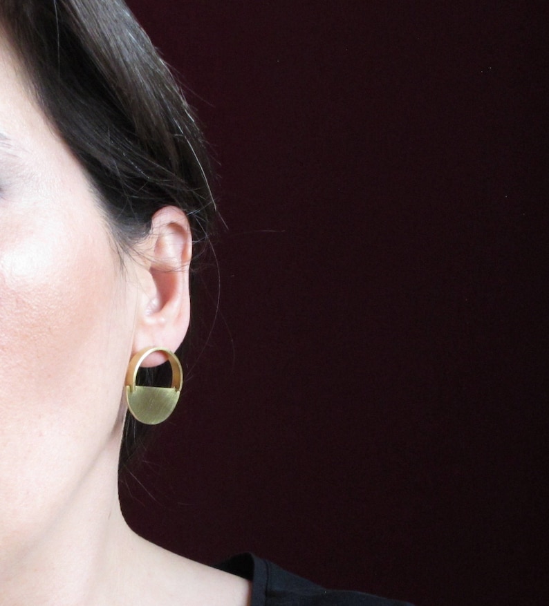 May include: A pair of gold-toned earrings with a half-circle design. The earrings are simple and modern.