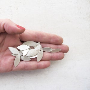 May include: A pile of silver leaf-shaped metal pieces in a hand.
