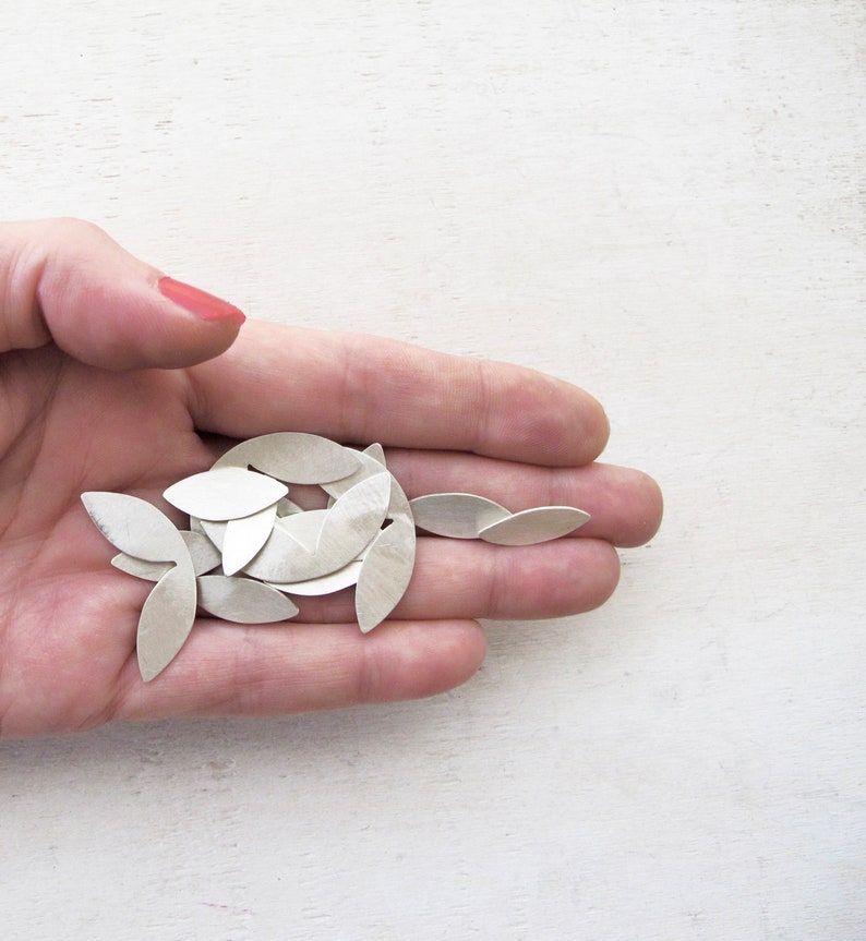 May include: A pile of silver leaf-shaped metal pieces in a hand.