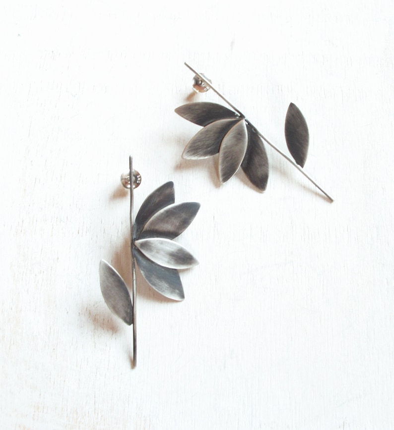May include: A pair of silver earrings with a flower design. Each earring features a stem with a single leaf and a flower with five petals.