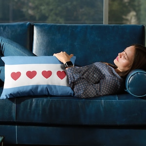 May include: A woman is relaxing on a blue couch with a pillow featuring the Chicago flag with red hearts.