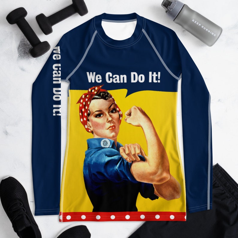 以下が含まれることがあります： 赤いバンダナをした女性と「We Can Do It!」という文字が描かれたヴィンテージイラストが、黄色い背景に描かれた紺色の長袖シャツ。首と袖には白とグレーのトリムが施されています。