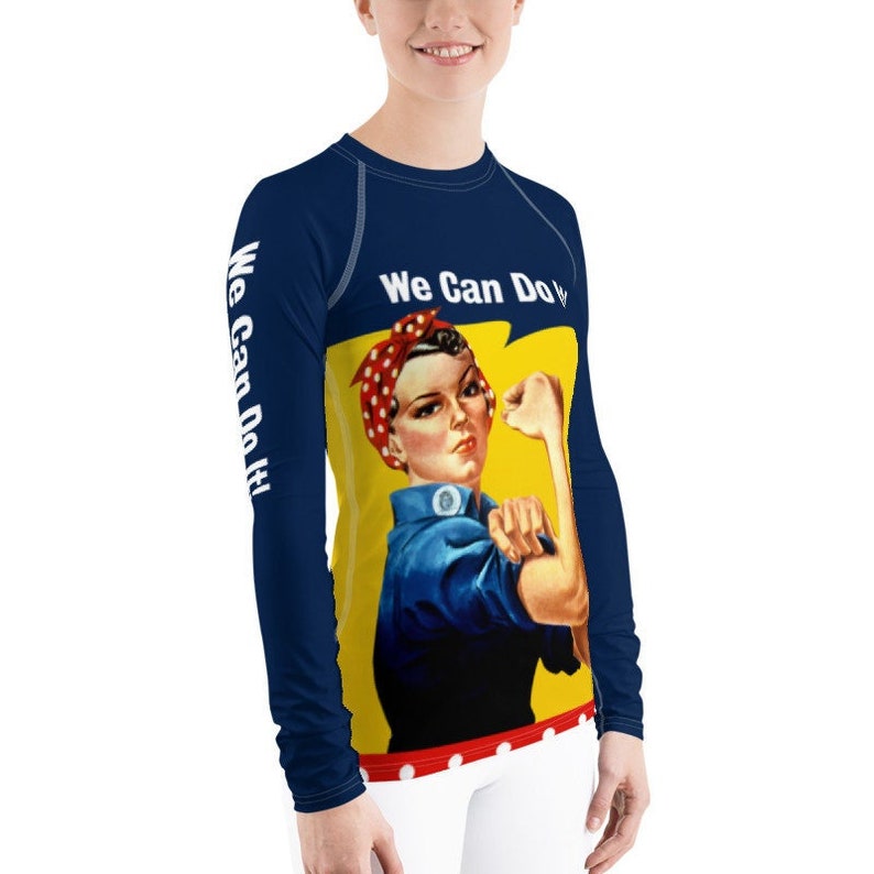 May include: A blue long-sleeved shirt with a yellow background image of a woman with her fist raised in the air. The woman is wearing a blue shirt and a red polka dot bandana. The text 'We Can Do It!' is written in white on the shirt.