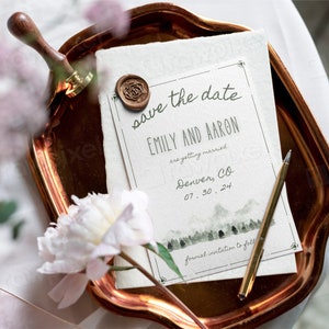 May include: A copper-colored tray holds a wedding invitation with the text "save the date" and the names "EMILY AND AARON." A gold pen and a wax seal with a rose design are also on the tray. A peony flower and a wax stamp are in the foreground.