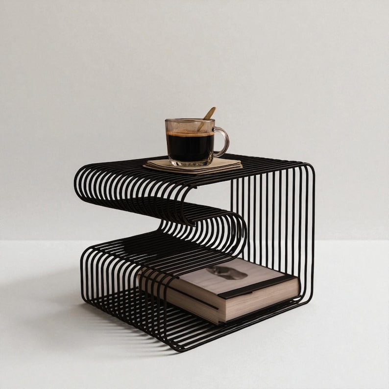 May include: A black metal side table with a unique, wavy design. A clear glass cup of coffee with a wooden spoon rests on top, along with a small stack of coasters. A book is placed on the lower shelf.