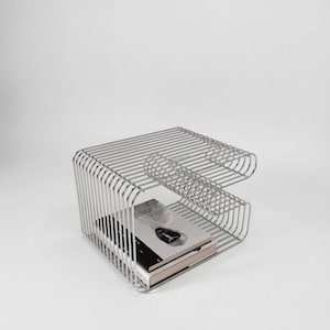 May include: A modern, silver-colored wireframe side table with a rectangular shape. The table features a shelf holding two books. The design incorporates curved elements and a minimalist aesthetic, suitable for contemporary decor.