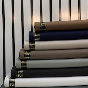 May include: A stack of eight fabric rolls in various colours, including brown, navy blue, beige, grey, and black. The fabric rolls are labelled "SULTAN" and "SULTANAM" with the text "England" printed on the label. The text "Grp B" is printed below the fabric rolls.