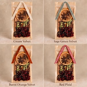 May include: Four clear pouches containing dried orange slices, star anise, cinnamon sticks, green cardamom pods, and dark red berries. Each pouch features a decorative ribbon loop in cream velvet, sage green velvet, burnt orange velvet, or red plaid.