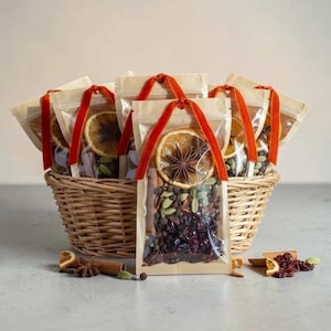 May include: A woven wicker basket filled with clear pouches containing dried orange slices, star anise, green cardamom pods, and dark red cranberries. Each pouch is tied with a vibrant red velvet ribbon. Loose spices and fruit are scattered nearby.
