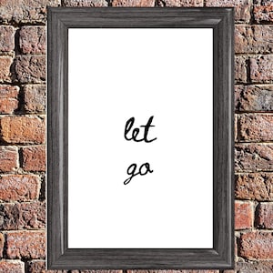 May include: A framed print with the words "let go" in black script on a white background. The frame is a dark gray color, and the background is a brick wall.