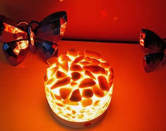 May include: A white night light shaped like a rock with a warm orange glow. The light is surrounded by two black butterfly-shaped decorations.