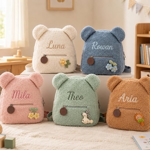 May include: Five plush bear-shaped backpacks in cream, blue, pink, sage green, and tan. Each bag features a front zippered pocket with a round pull, embroidered names Luna, Rowan, Mila, Theo, and Aria, and small decorative floral or animal appliques.