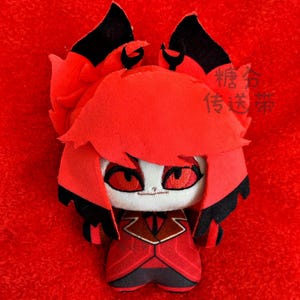 May include: A plush doll with a red and black color scheme. The doll has a stylized design with large red eyes, a white face, and a red outfit. The doll's hair and ears are also red and black.