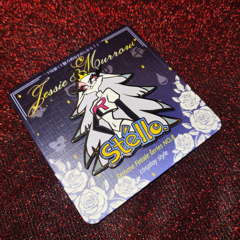 May include: A pin featuring a stylized character with long gray hair and a crown, wearing a white and black outfit with a red "R" emblem. The pin is on a dark blue card with white roses and text that reads "Jessie & Mourrow" and "Stella."