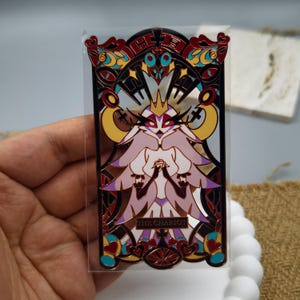 May include: A gold and red metal bookmark with a detailed design featuring a figure with a crown and wings. The bookmark has the text "THE CHARIOT" at the bottom.