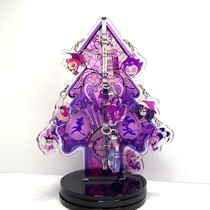 May include: A purple and pink acrylic Christmas tree ornament featuring various cartoon characters. The ornament is on a black stand.