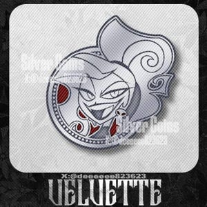 May include: A silver-colored pin featuring a stylized character design with a grinning face, red accents, and a skull earring. The pin has a circular border with a dotted pattern and the text "Silver Coins". The word "VELVETTE" is at the bottom.