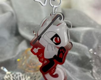 Könnte beinhalten: Ein klarer Acryl-Schlüsselanhänger mit einer Cartoonfigur mit weißem Körper, roten Akzenten und einer schwarzen Pfote. Der Schlüsselanhänger hat eine weiße Schleifenform und einen silberfarbenen Verschluss.