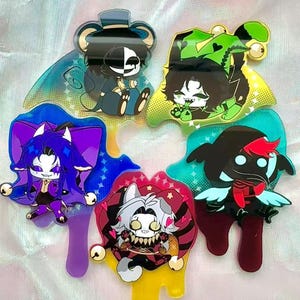 Pode incluir: Uma coleção de pingentes de acrílico coloridos com personagens de desenhos animados com designs exclusivos. Cada pingente tem uma forma e esquema de cores distintos, incluindo azul, roxo, verde, vermelho e amarelo. Os pingentes têm um acabamento brilhante.