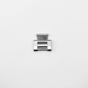 May include: A small, silver-coloured metal clasp with a rectangular base and a hinged top. The clasp has a series of horizontal bars across the centre. The object is centred on a white background.