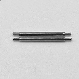 May include: Two small, silver-colored watch spring bars are displayed against a white background. Each bar has a cylindrical center section with a smaller pin extending from each end. These are likely watch repair components.