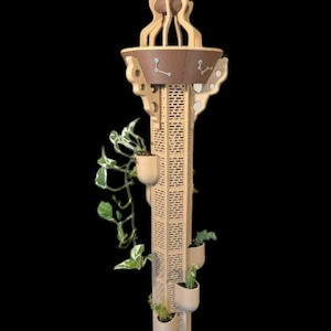 May include: A decorative wooden plant stand with a tower design. The stand features a brown top with a pointed finial and several small planters for displaying plants. The stand is beige with a geometric pattern and has a black background.
