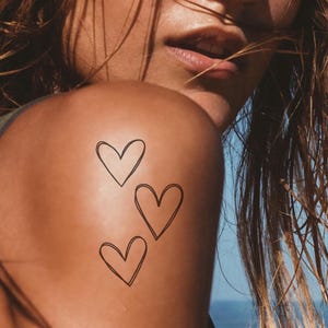 May include: Three simple line drawings of hearts on a person's shoulder.