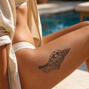 May include: A temporary tattoo featuring a black ink illustration of a seashell. The shell design is filled with intricate geometric patterns, including cross-hatching, dots, and lines, creating a detailed and decorative artistic motif on the skin.