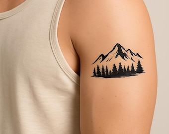 May include: A black temporary tattoo design featuring a mountain range with sharp peaks positioned above a dense forest of pine trees. The graphic is rendered in a solid black ink style with clean lines and a high contrast appearance on the skin.