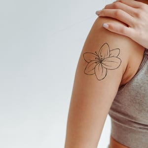 May include: A close-up of a person's arm with a simple line drawing tattoo of a flower on the upper arm.