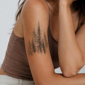 May include: A temporary tattoo design featuring a cluster of dark brown pine trees with detailed needle textures and a stippled base effect. The artwork is applied to the upper arm, showcasing a dense forest scene with varying tree heights.