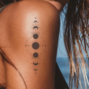 May include: A woman's shoulder with a temporary tattoo of a geometric design featuring a crescent moon, a full moon, and a star.