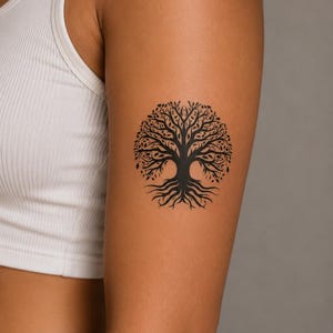 May include: A black temporary tattoo featuring a detailed tree of life design with intricate branches, leaves, and exposed roots. The circular illustration is applied to the upper arm, showcasing a symmetrical pattern with a solid trunk and canopy.