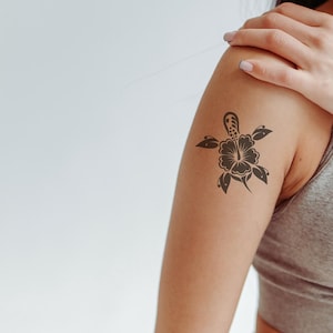 Puede incluir: Un tatuaje en blanco y negro de una tortuga con una flor en la espalda. El tatuaje está en el brazo de una persona.