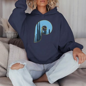 Könnte beinhalten: Ein marineblauer Kapuzenpullover mit einem großen blauen und gelben 'P' auf der Vorderseite. Das 'P' ist mit einer Skyline-Silhouette gefüllt.