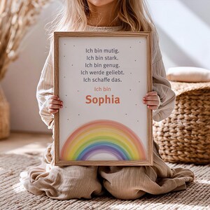 Könnte beinhalten: Ein gerahmter Druck mit einem Regenbogen und dem Text "Ich bin mutig. Ich bin stark. Ich bin genug. Ich werde geliebt. Ich schaffe das. Ich bin Sophia." Der Druck hat einen Holzrahmen und wird gehalten.