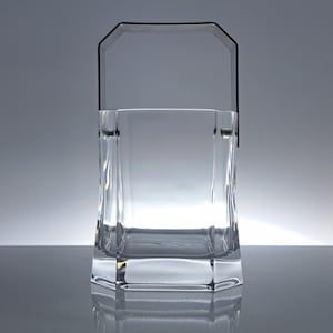 May include: A clear, faceted glass ice bucket with a black handle. The bucket has a rectangular shape with a geometric base and a handle that arches over the top. The glass is transparent, allowing light to pass through.