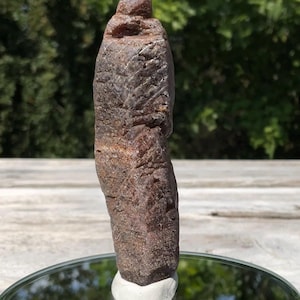 May include: A tall, elongated, raw crystal specimen with a rough, textured surface in shades of deep reddish-brown and dark burgundy. The stone features a vertical, columnar structure with natural striations and a rounded, slightly tapered top.