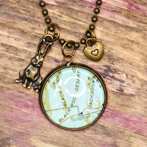 May include: A necklace with a round pendant featuring a vintage map of Black Rock Desert, Sulphur, and Jackson, with a bronze rabbit charm and a heart charm.