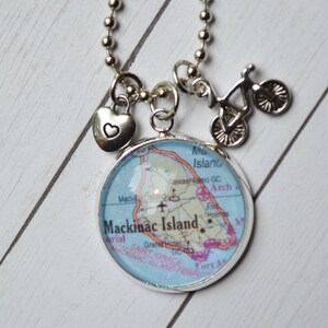 Op de afbeelding: Een zilveren ketting met een bedel met een kaart van Mackinac Island, Michigan. De ketting heeft ook een klein hartbedel en een fietsbedel.